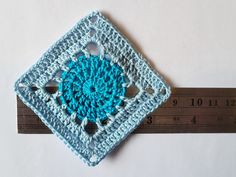 a crocheted square with a hole in the middle and a ruler behind it