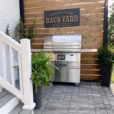 an outdoor bbq area with stairs leading up to the back yard sign and potted plants