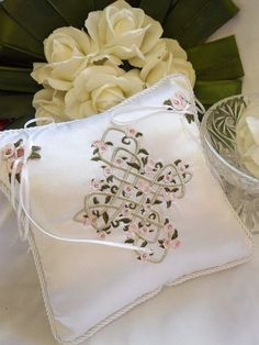 a white pillow sitting on top of a table next to flowers and a glass vase