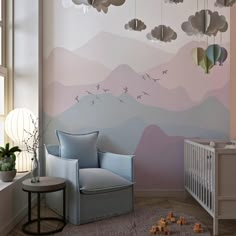 a baby's room decorated in pastel colors with mountains and clouds painted on the wall