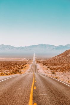 an empty road in the middle of nowhere with mountains in the background