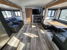 the interior of an rv with wood flooring and couches, windows, and kitchen