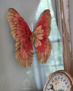 a clock with wings hanging from it's side next to a wall mounted thermometer