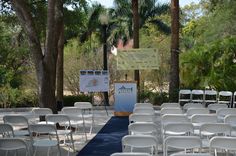 rows of white chairs are set up for an outdoor ceremony in front of palm trees