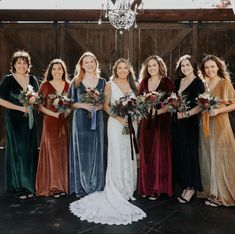 a group of women standing next to each other holding bouquets in front of a barn