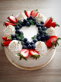 a white cake topped with berries and blueberries on top of a wooden table next to a knife