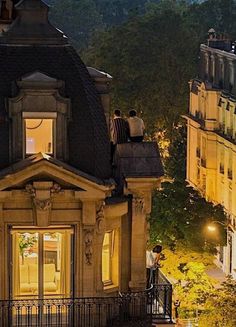 two people are sitting on the roof of a building at night, looking out into the city