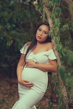 a pregnant woman leaning against a tree with her hands on her stomach and looking at the camera