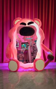 a pink teddy bear car with wheels and lights in front of a red stage curtain