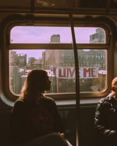 two people sitting on a bus looking out the window with love me written on it