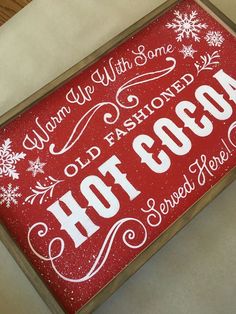 a red hot cocoa sign with white lettering and snowflakes on the bottom says, warm with some old fashioned hot cocoa