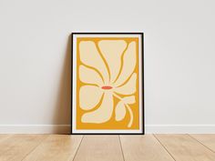 an orange and yellow flower on a white background in a black frame against a wall