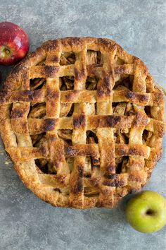 an apple pie next to two apples on a table