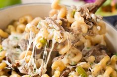 a spoon full of macaroni and cheese being lifted from a bowl with meat