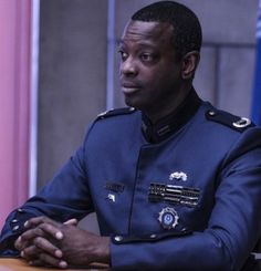 a man in uniform sitting at a table with his arms crossed and looking off to the side