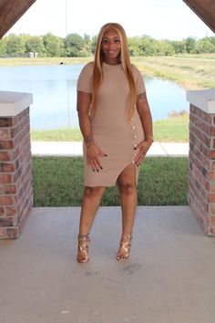 a woman standing in front of a brick wall with her hands on her hips and legs crossed