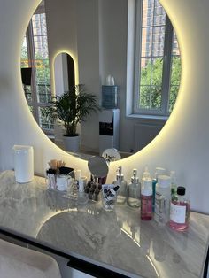 a bathroom vanity with a round mirror above it and various bottles on the counter top