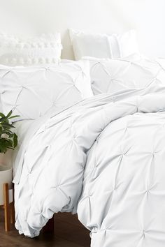 a bed with white comforter and pillows in a room next to a potted plant