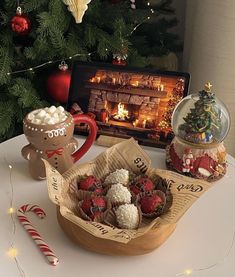 a table topped with a basket filled with chocolate covered strawberries next to a christmas tree