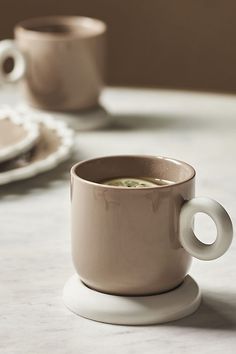 two coffee mugs sitting on top of a white table next to plates and napkins