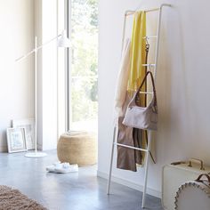 a white coat rack with clothes hanging on it next to a window and a suitcase