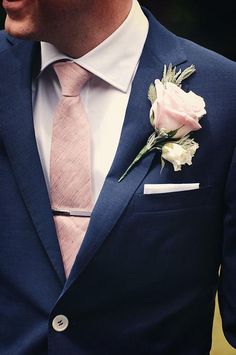 a man wearing a blue suit with a pink tie and white rose boutonniere