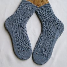 two pairs of blue knitted socks sitting on top of a wooden paddle holder next to a white sheet