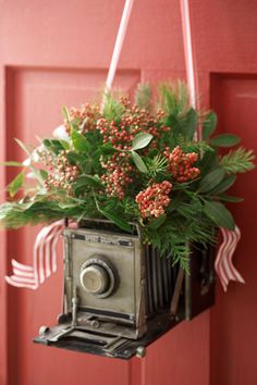 an old camera hanging from a red door with flowers in it and ribbon on the handle