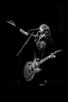 a man with long hair holding a guitar and singing into a microphone while standing on stage