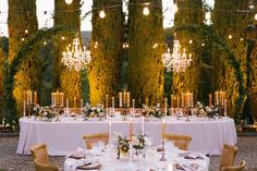 an outdoor dinner table set up with candles, flowers and greenery in the background