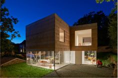 a modern house is lit up at night with people sitting on the lawn and outside