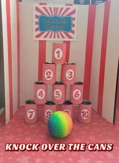 a colorful ball sitting in front of a display with numbers on it and the words knock over the cans