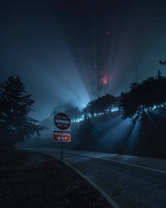 a street sign sitting on the side of a road under a foggy night sky