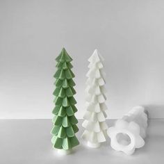 three ceramic christmas trees sitting next to each other on a white counter top, one is green and the other is white