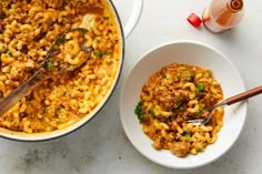 two bowls filled with macaroni and cheese next to a bottle of orange juice