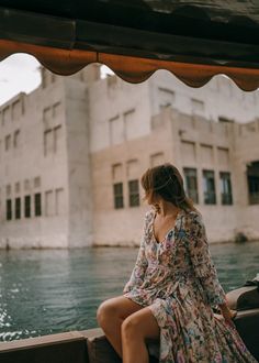 a woman sitting on the back of a boat in front of a building and water