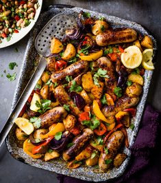 a platter filled with sausages and vegetables next to a bowl of lemon wedges