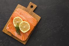 a piece of salmon with lemons and dill on a cutting board