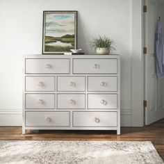 a white dresser sitting on top of a hard wood floor next to a wall with a painting above it