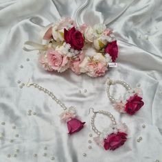 the bridal bouquet and jewelry are laid out on a white satin bed sheet with pearls