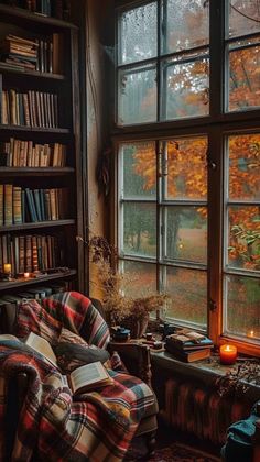 a living room filled with lots of books and furniture next to a window covered in fall leaves