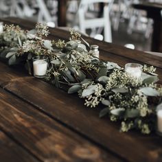 candles and greenery are lined up on a wooden table