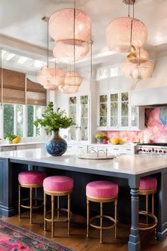 a large kitchen with pink stools in front of the island and windows above it