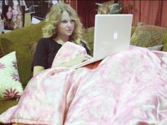 a woman sitting on a couch with a laptop in her lap and covered by a pink blanket