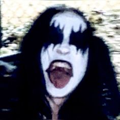 a person with black hair and white makeup is making an open mouth while standing in front of a blurry background