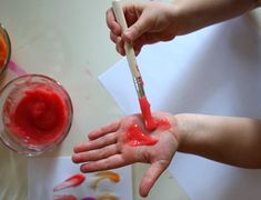 two hands with red paint on them and one hand holding a brush over the other