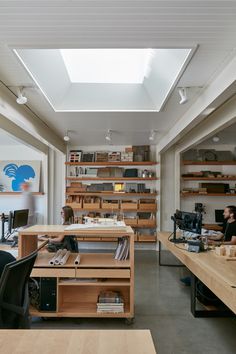 two people sitting at desks in an office with skylight above them and shelves full of books