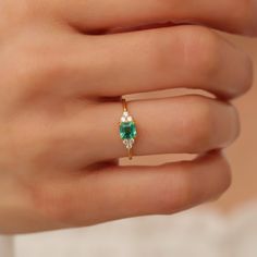 a woman's hand wearing a ring with an emerald and diamond