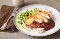 a white plate topped with green beans and meat covered in sauce on top of rice