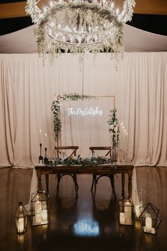 a table with candles and flowers on it in front of a chandelier that says the wedding